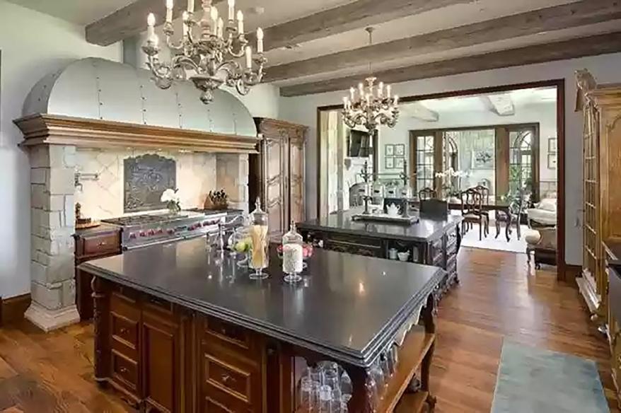 The kitchen has hardwood floors and a large stone-columned hood over the industrial oven and stove.