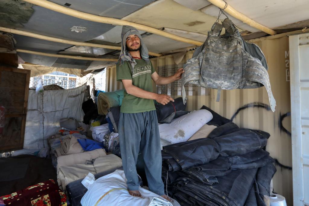 An Afghan scrap dealer named Keramatullah, 19, poses for a photograph as he shows a US military armor vest among the items which were discarded by the US forces outside Bagram Air Base