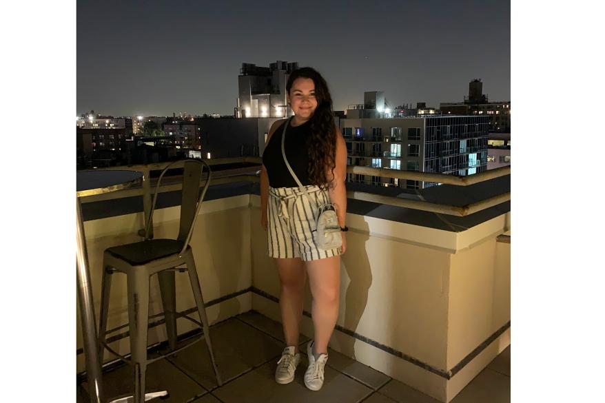 Sophie Cannon stands on a rooftop wearing white and gray striped shorts and a black top