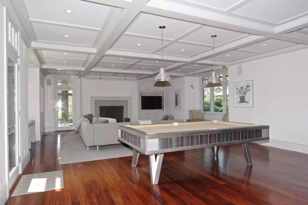 This entertainment room has coffered ceilings, a fireplace and is positioned with a pool table.