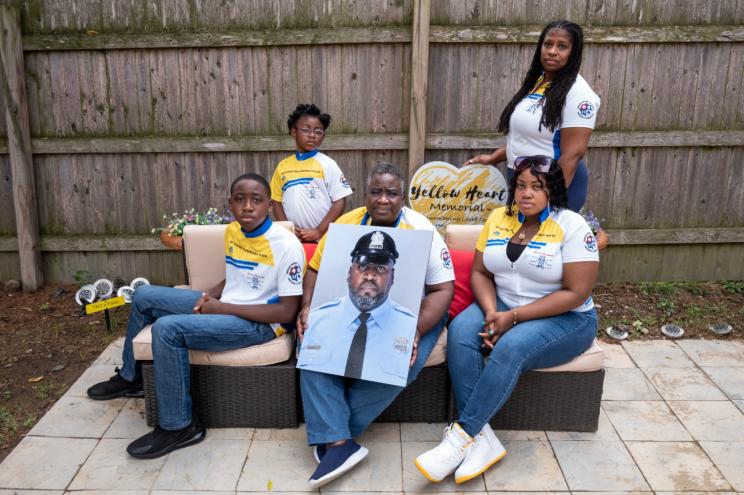 Octavia Tokley standing right, along with her mother-in-law, Ikelyn, step-daughter 21 year old Tamaira, step-son 12-year old XavierSunday, and daughter Amethyst, five years old, pose with a portrait of Erin "Toke" Tokley, a Philadelphia cop who died from COVID-19 in March, on Aug. 29, 2021, in Secane, Pa.