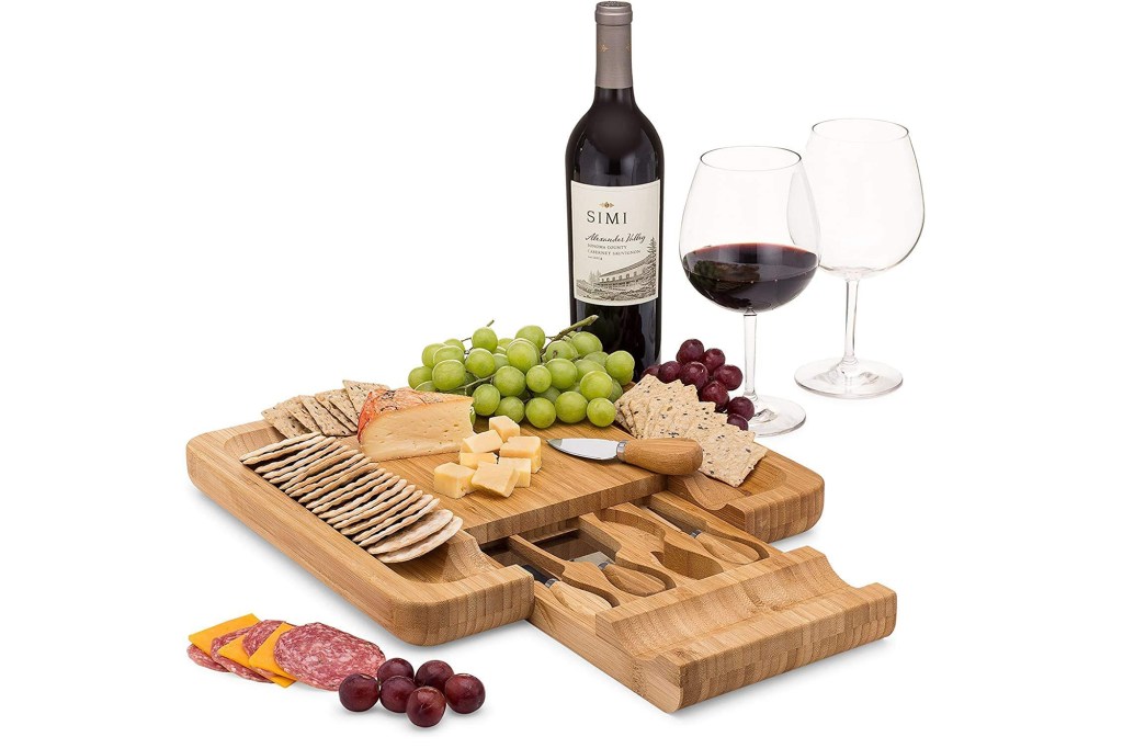A wooden cheese board with food on it and wine 
