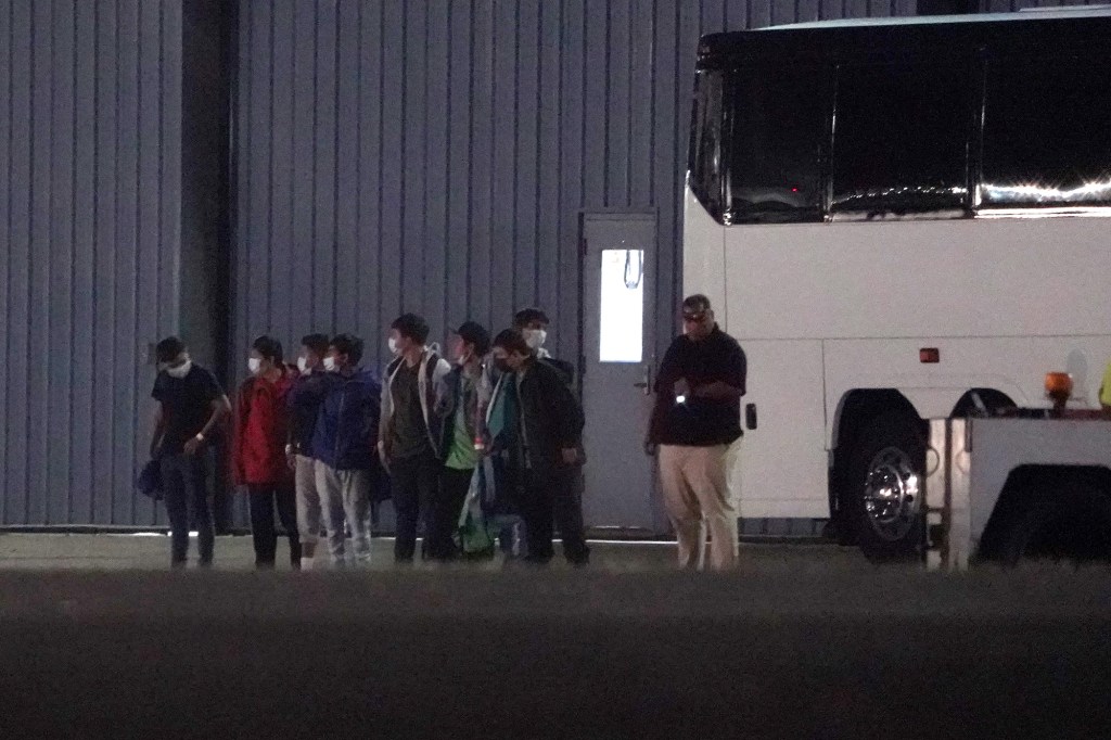 Masked immigrants are lined up outside a bus at Westchester County Airport.