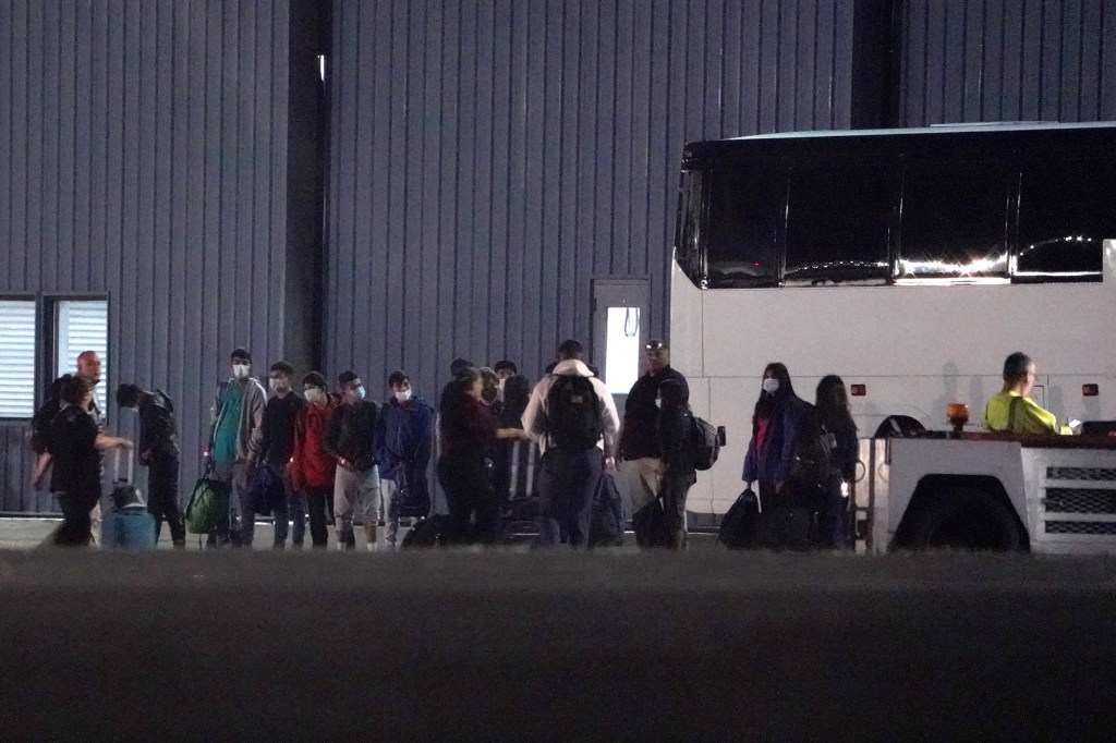 Immigrants from the southern border wait alongside a charter bus at Westchester County Airport in White Plains.