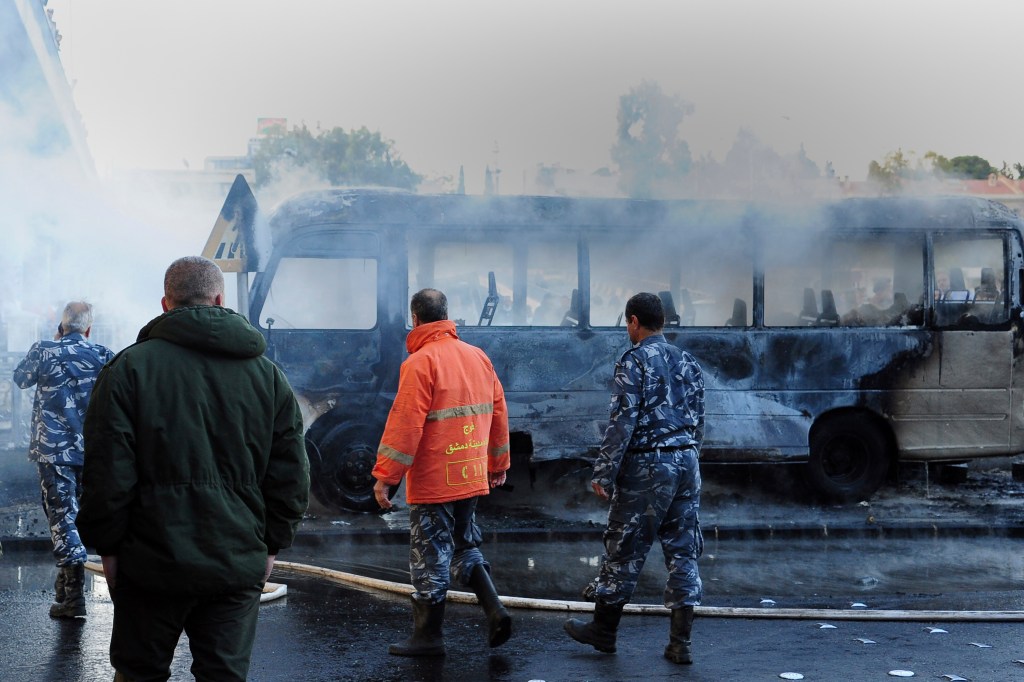 Firefighters and security officers check a burned bus at the site of a deadly explosion.