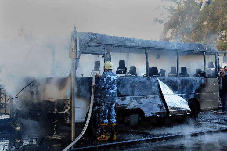 A Syrian firefighter extinguishes a burned bus at the site of a deadly explosion, in Damascus.