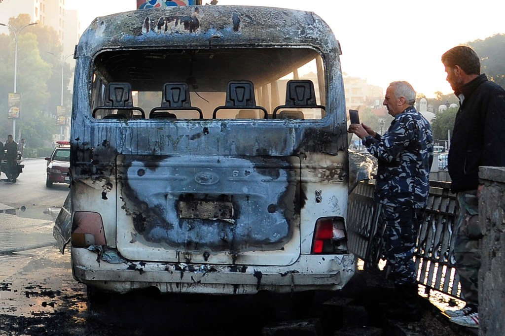 Syrian security officers gather around a burned bus at the site of a deadly explosion.