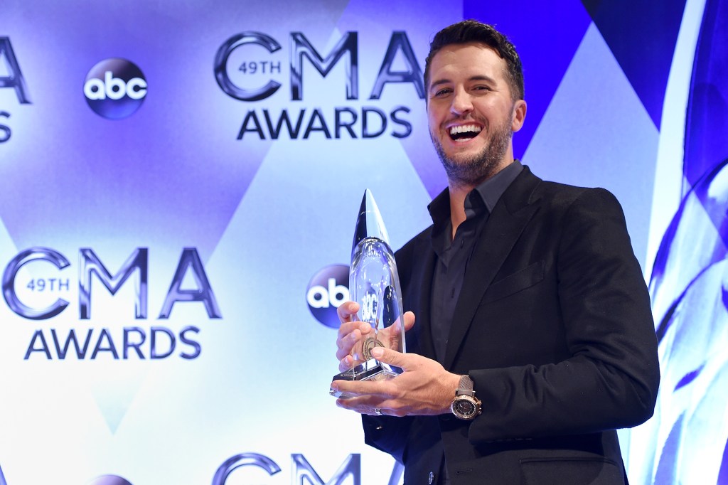 Luke Bryan holds an award and stands in front of an ABC banner. 