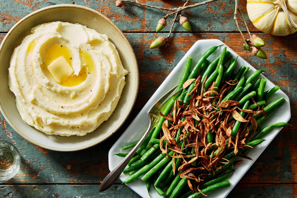 A bowl of mashed potatoes and a plate of green beans with almonds 