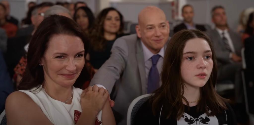 Charlotte sits with child, other actors behind her.