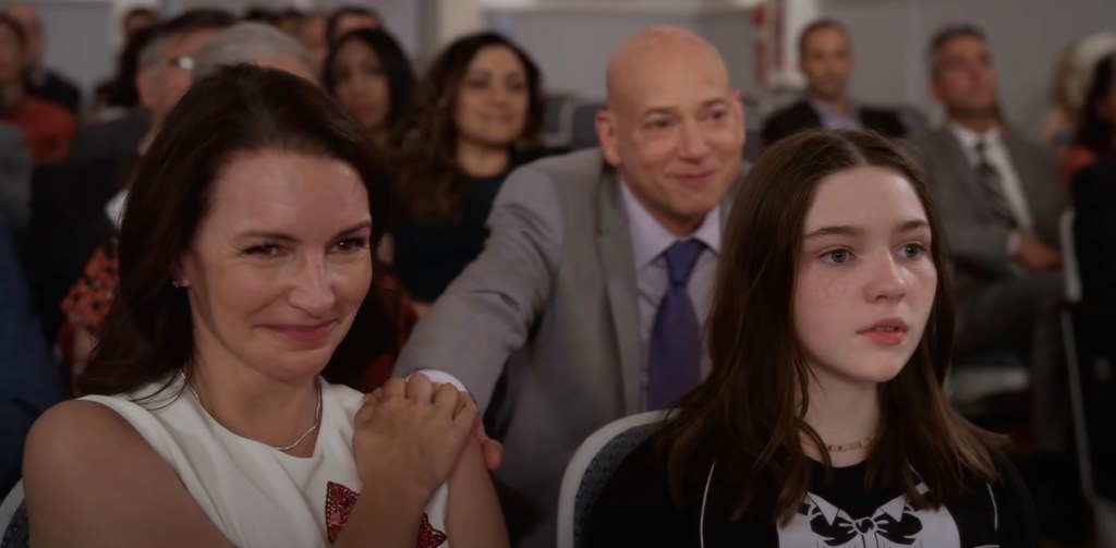 Charlotte sits with child, other actors behind her. 