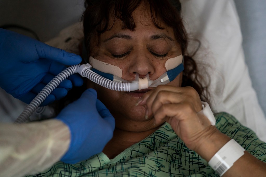 Respiratory therapist Frans Oudenaar replaces an oxygen tube for Linda Calderon in a COVID-19 unit at Providence Holy Cross Medical Center in Los Angeles.