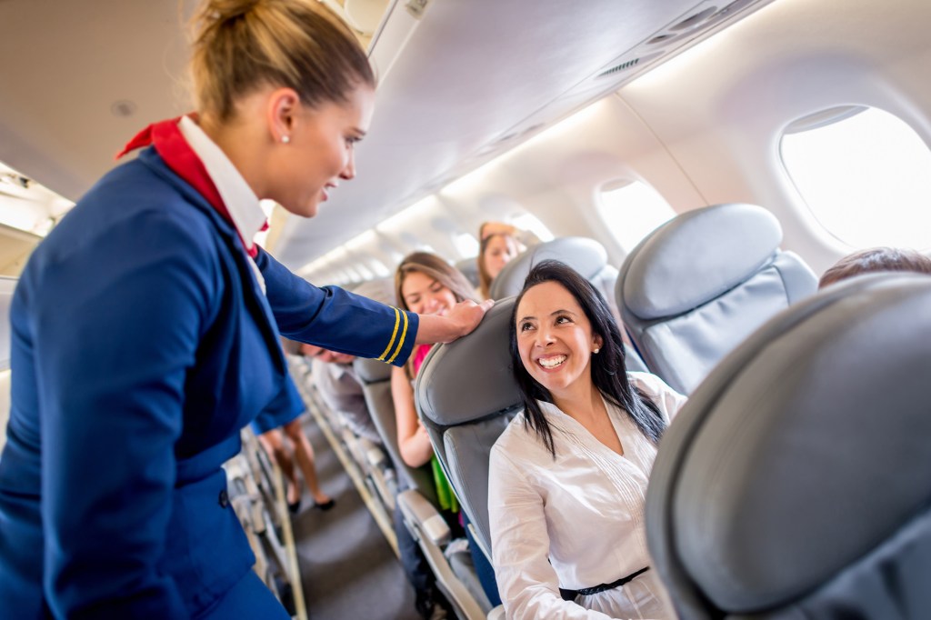 A flight attendant and passenger exchange smiles.