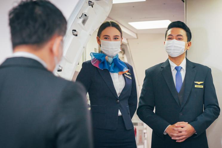 Flight attendant and cabin crew wearing a face mask working on board during pandemic.