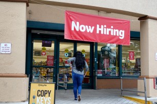 A person enters a supermarket that has a Now Hiring sign above the entrance