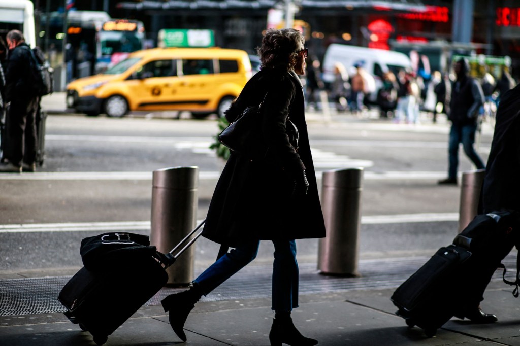 A woman walks with a carry on suitcase in midtown New York City.