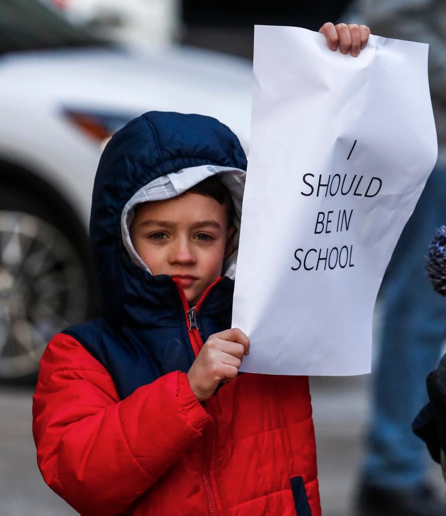 A young boy stands outside protesting with family