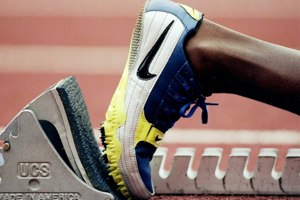 A runner wearing a Nike shoe stands in the starting blocks before a race