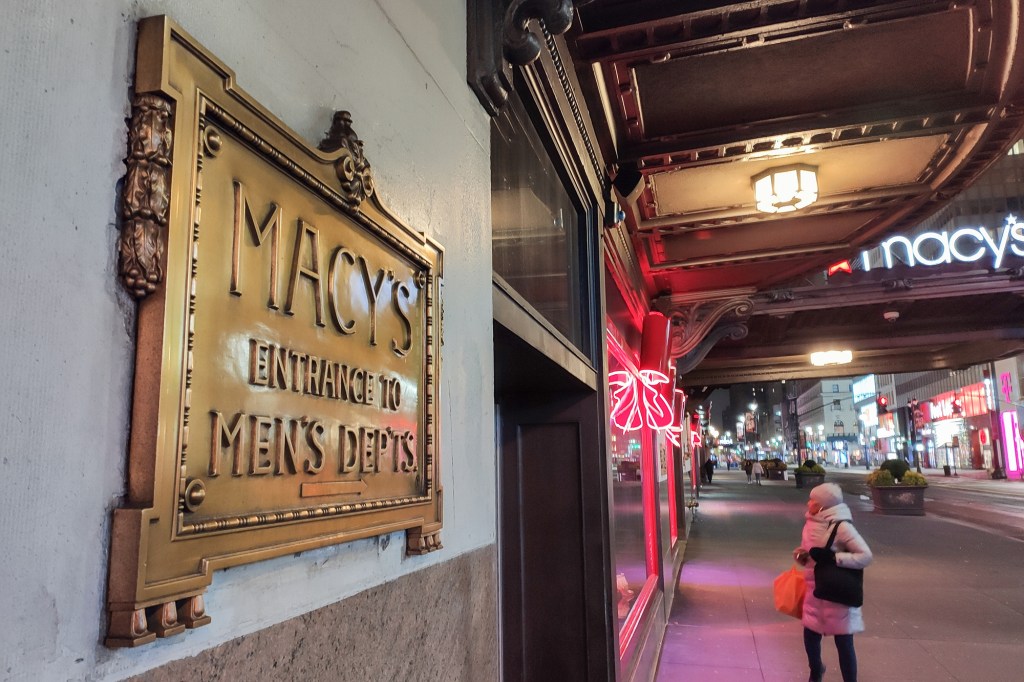 A woman in winter clothes peers in the window outside Macy's