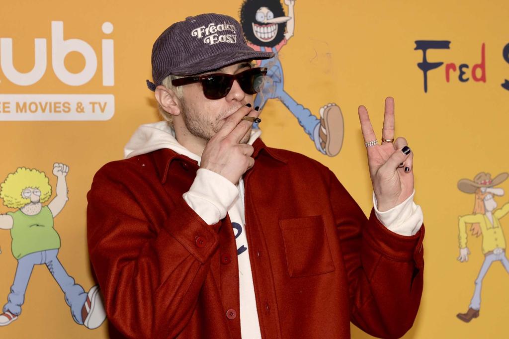 Pete Davidson holds up the peace sign as he takes a drag from a cigarette.