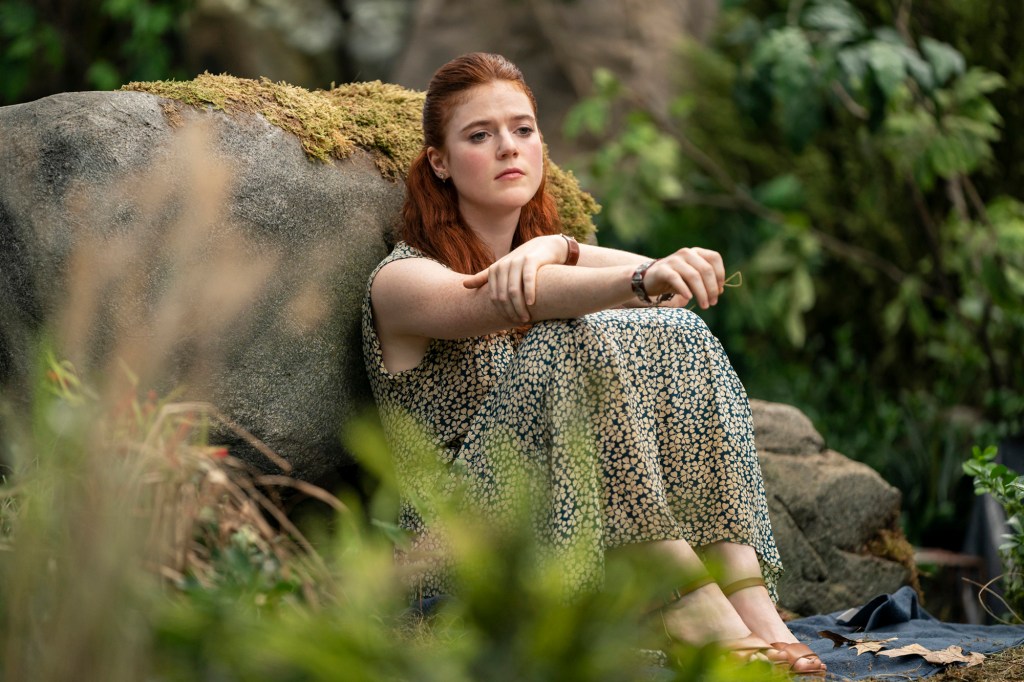 Rose Leslie leans against a rock looking sad. 