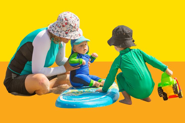 mom and babies playing on the beach in sun protective clothing