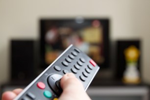 A hand points a remote at a TV.