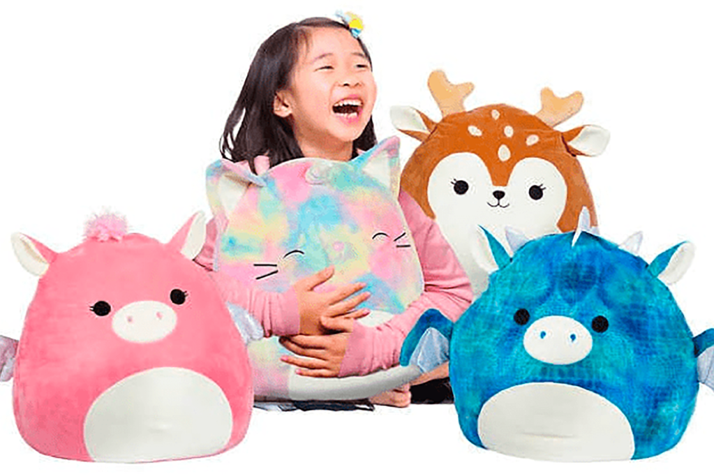 A child smiling next to four Squishmallow plushies 