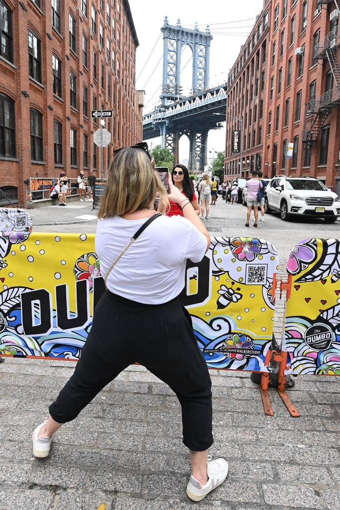 A woman takes a photo of a friend posing in front of the Manhattan Bridge on Washington Street.