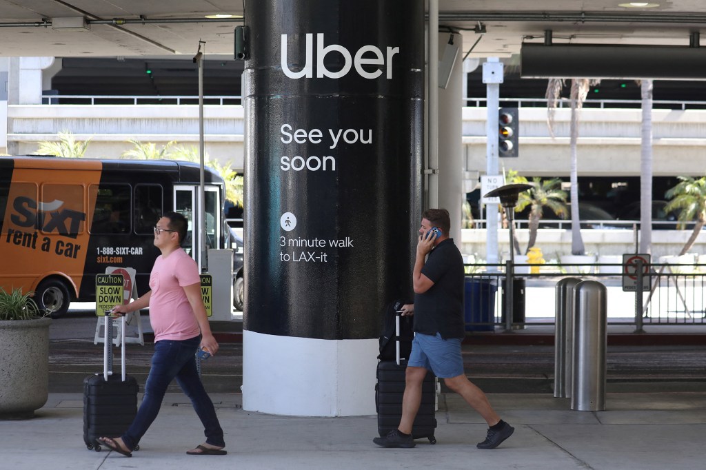 Passengers walk near Uber ride-share signage.
