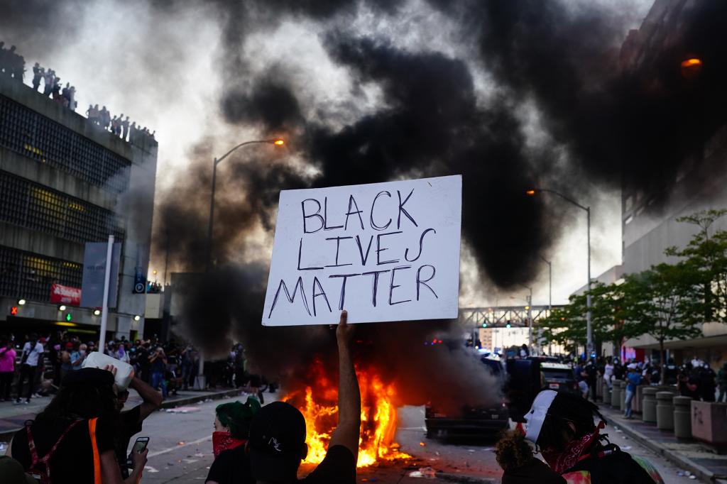 A man holds a Black Lives Matter sign as a police car burns during a protest on May 29, 2020 in Atlanta, Georgia. Demonstrations are being held across the US after George Floyd died in police custody on May 25th in Minneapolis, Minnesota.