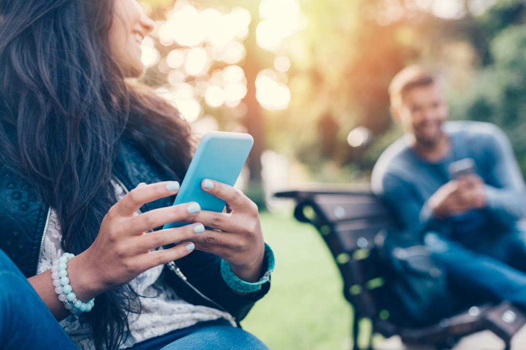 Happy couple using smartphones in the city park.