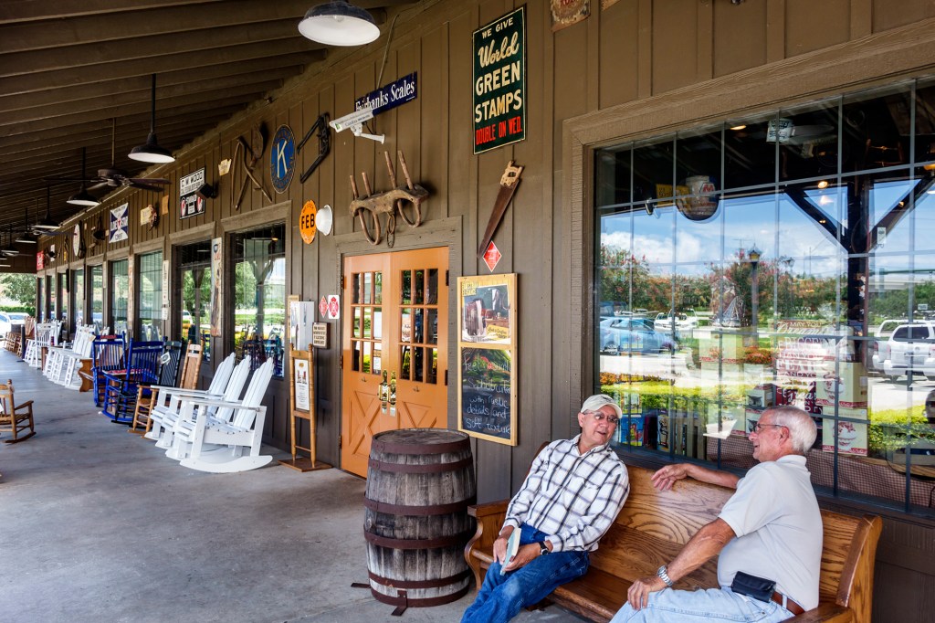 Two older men sitting on a bench in front of a Cracker Barrel.