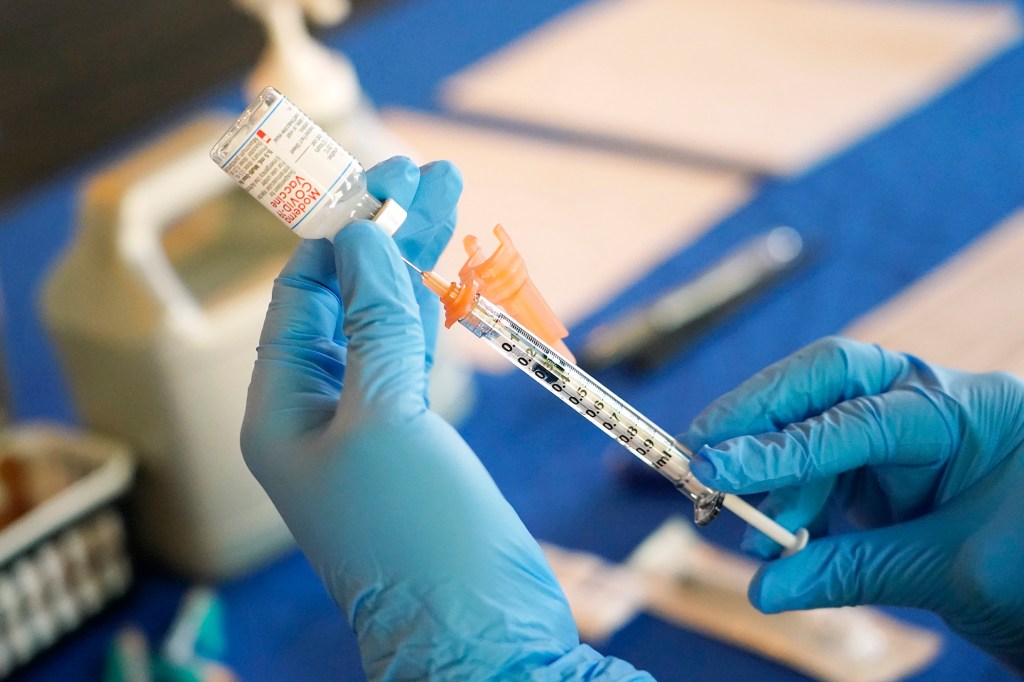 A gloved hand is shown loading up a COVID-19 vaccine into a syringe 