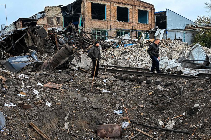 People stand by a crater left near a railway yard of the freight railway station in Kharkiv, which was partially destroyed by a missile strike, amid the Russian invasion of Ukraine on September 28, 2022.