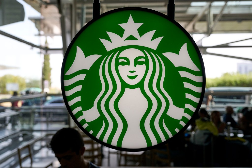 Travelers are silhouetted while sitting under Starbucks Coffee logo in the arrivals hall at Terminal 1 in Humberto Delgado International Airport Humberto Delgado International Airport on October 07, 2022 in Lisbon, Portugal