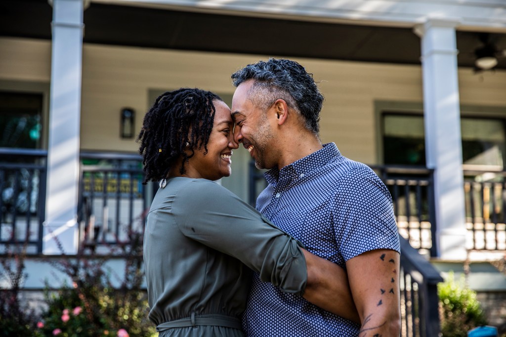 Husband and wife embracing in front of new home.