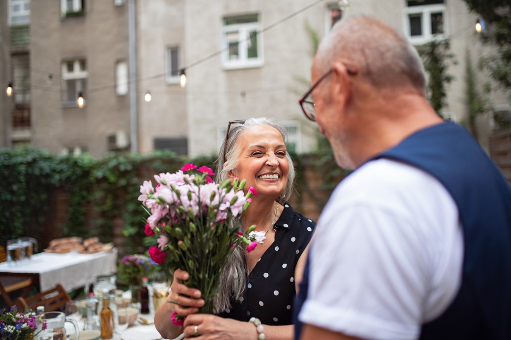 Senior man giving flowers to his wife at anniversary celebration outdoors at front or backyard.