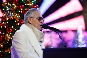 Andrea Bocelli sings and plays the piano in front of a lit up Christmas tree.