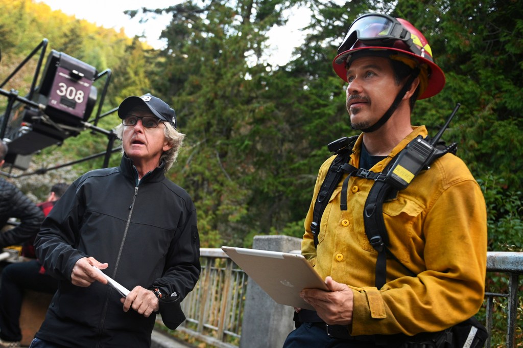 Kevin Alejandro in action directing Friday night's midseason finale of "Fire Country" on CBS. He's wearing Manny's yellow firefighter uniform and holding what looks like an iPad while he watches a scene.
