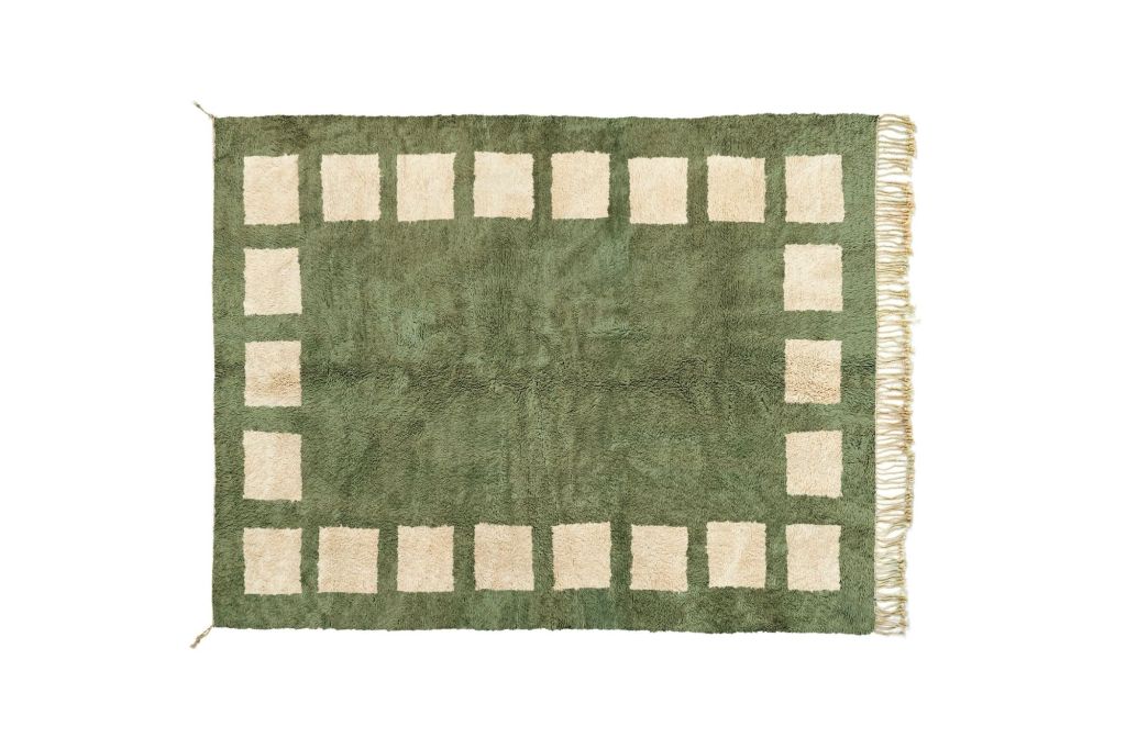 Green area rug with fringe and cream colored squares around the border.