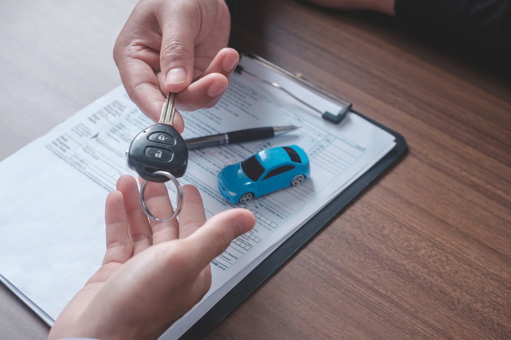 Concept car rental. Close up view Hand of agent giving car key to customer after signed rental contract form.