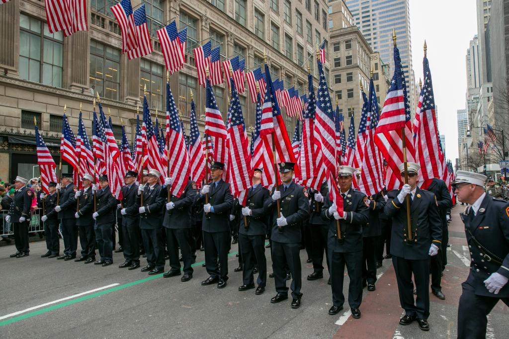 Members of the New York City Fire Department carry American flags in front of similar flags hanging on a building on 5th Avenue in New York City during the St. Patrick's Day Parade on Friday, March 17, 2023.