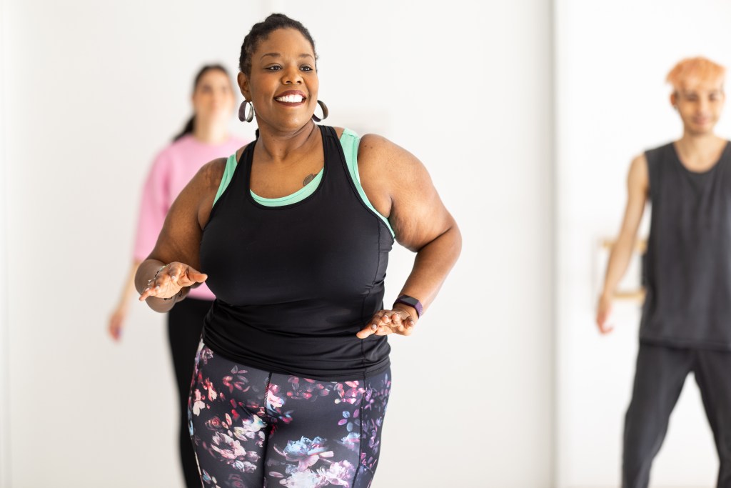 Smiling african woman enjoying dancing at a fitness studio. Group of people doing dance workout at health club.