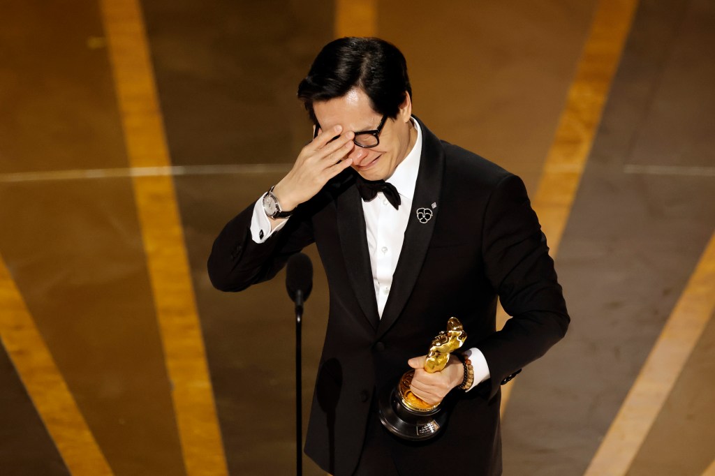 Ke Huy Quan holding an Oscar, crying. 