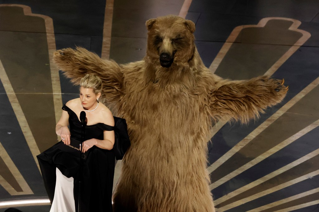 Elizabeth Banks standing onstage at the Oscars next to a bear. 