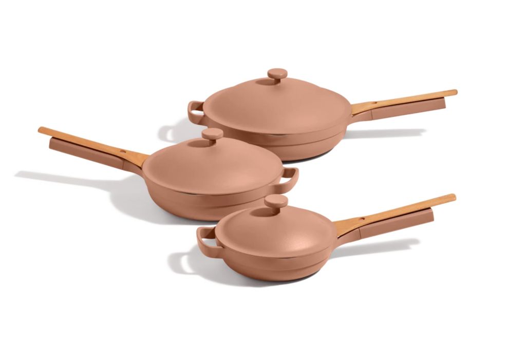 Three cooking pans in a row with lids, each in the color rose gold.