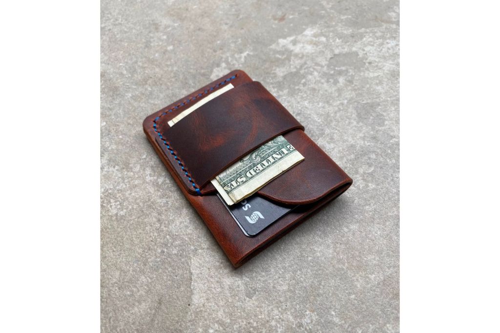 Brown leather wallet with strap and dollar bill tucked in.