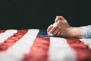 Hands praying over USA flag.