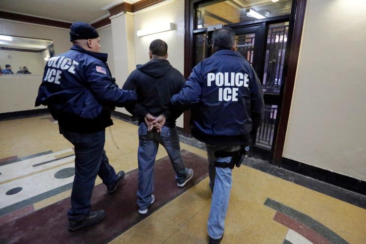 Immigration and Customs Enforcement officers escort an arrestee in an apartment building.